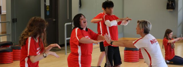 MOVE Coach in front of MOVE class showing MOVE participant correct form while participant is laughing
